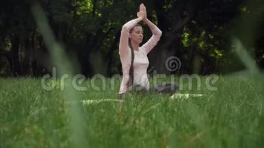 一位孕妇在公园里练习瑜伽，坐在莲花的位置，抱着她的手臂在上面冥想。